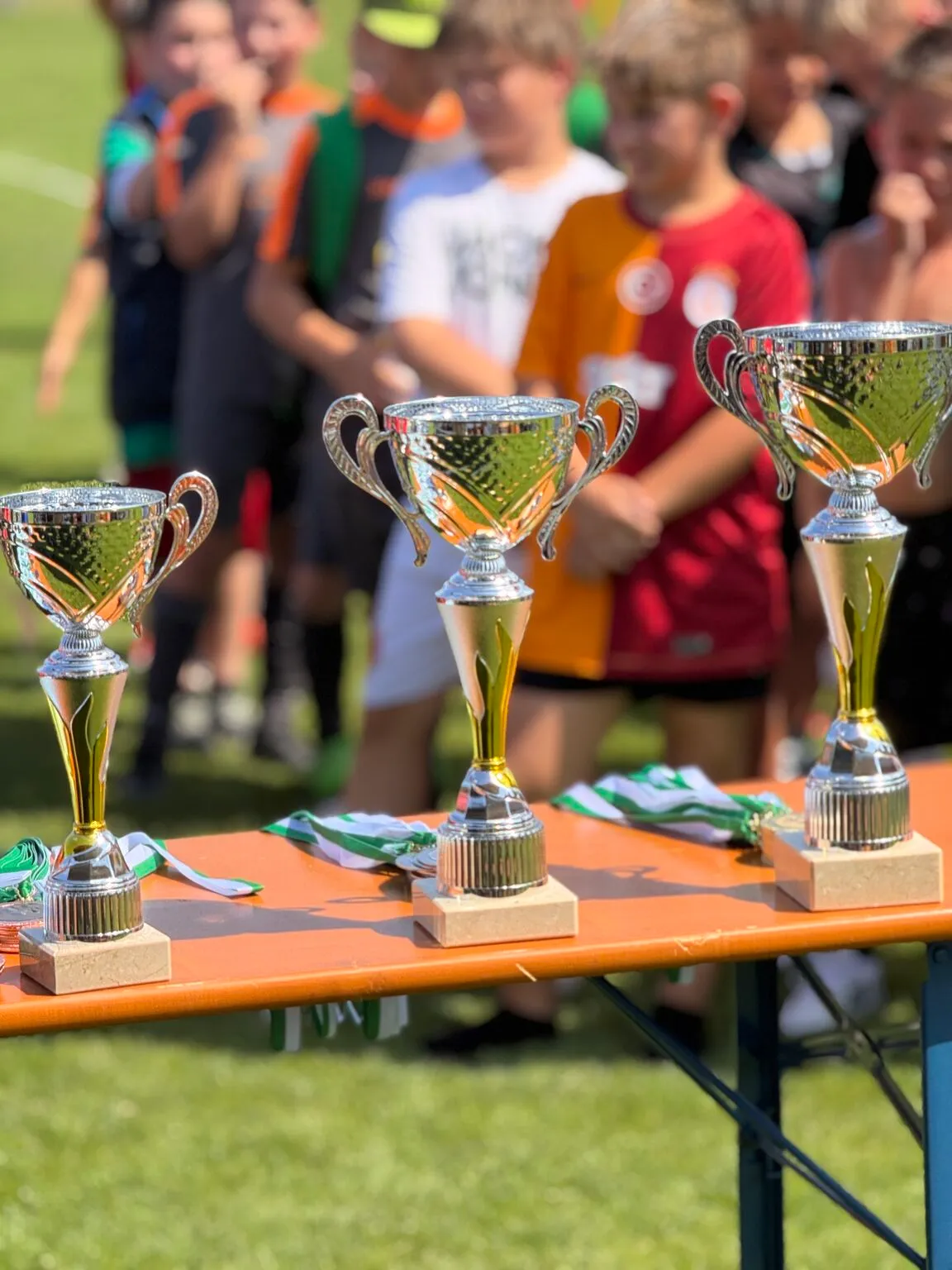 Drei Pokale für den CurveDesign Cup 2025 auf dem Fußballplatz des TSV Greding.